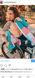 picture of author, shirtless, in wheelchair with trans flag towel